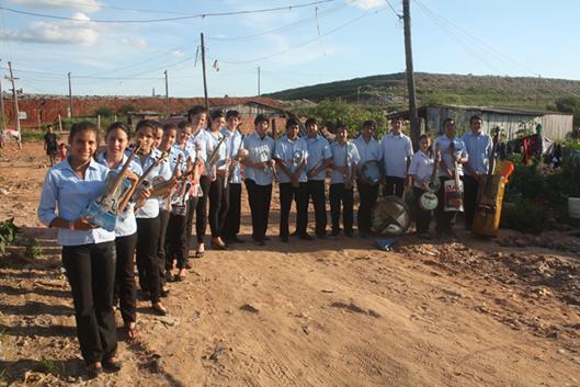 Young people wearing black pants and white shirts standing in a dusty landfill holding the musical instruments they&#39;ve created